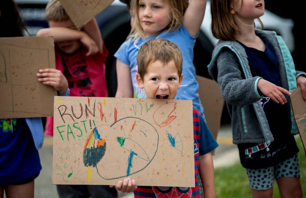 Young boy from the GVSU Children's Enrichment Center holding a handmade sign "Run Fast" sign as he pretends to bite the sign